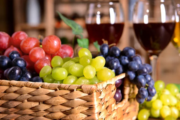 Grape in wicker box on a table on wine bottles background