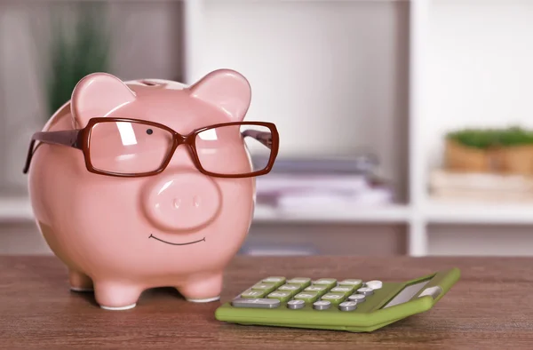 Piggy bank in glasses with calculator on home or office background