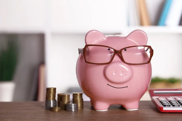 Piggy bank in glasses with calculator and coins on home or office background