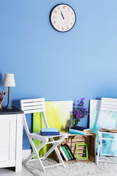 Room design with white furniture, bookcase, pictures, flowers and clock over blue wall