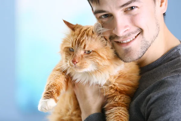 Smiling young man holding a fluffy red cat