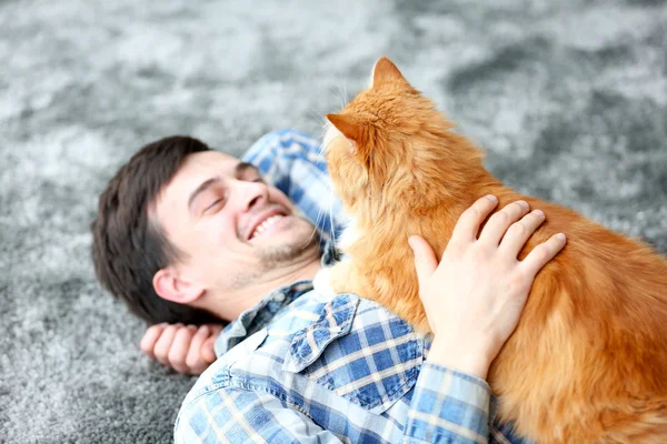 Young man with fluffy cat lying on a carpet