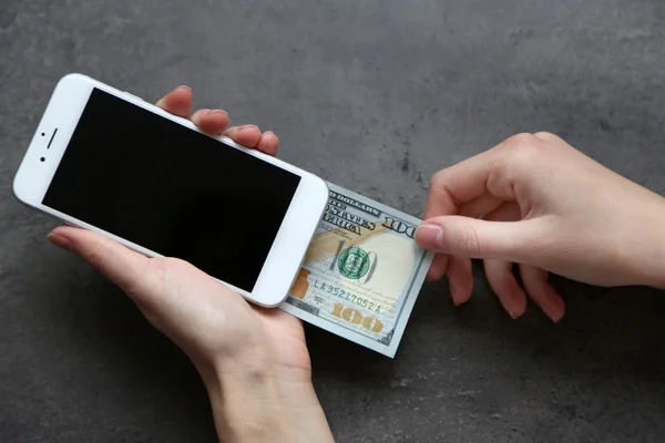 Hands holding smart phone with dollar banknote on grey background. Making money online