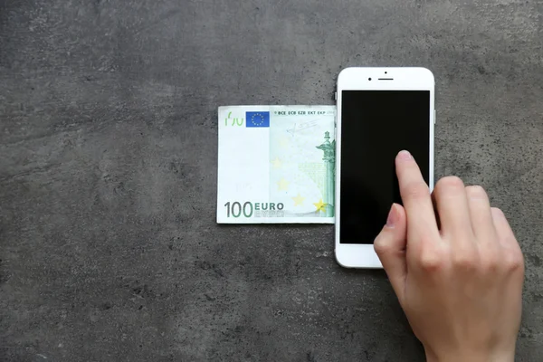 Hand with smart phone and euro banknote on grey background. Making money online