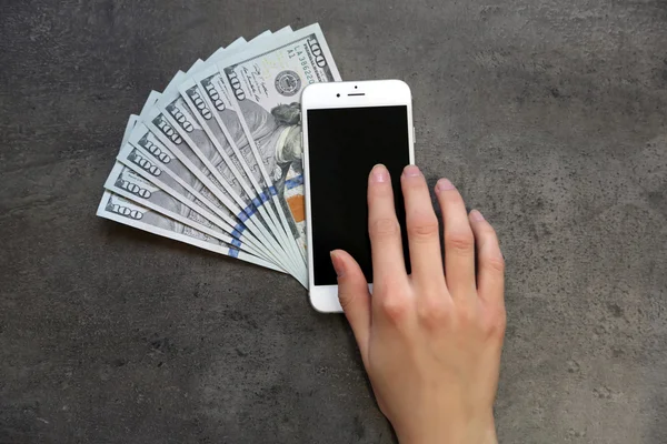 Hand with smart phone and dollar banknotes on grey background. Making money online
