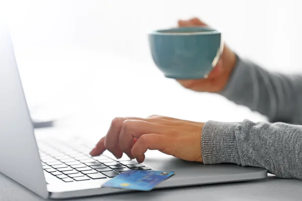 E-commerce concept. Woman with credit card, laptop and cup of coffee, close up