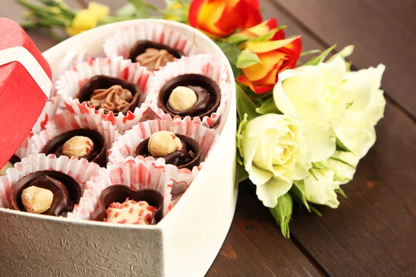 Heart shaped box with candies and flowers on a wooden background, close up