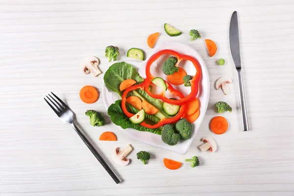 Useful cut vegetables on a plate in the form of heart on wooden table top view