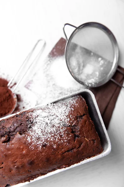 Chocolate cake in baking dish with powdered sugar on white table