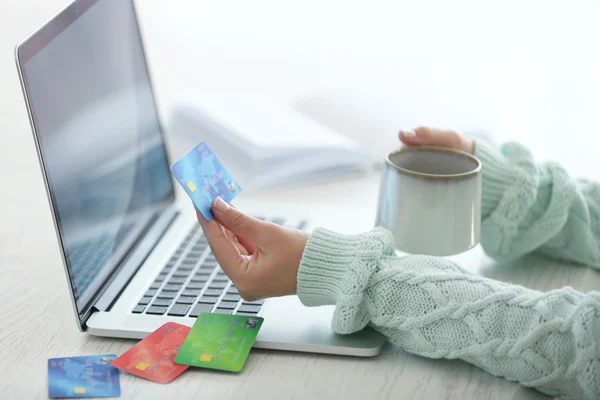 E-commerce concept. Woman with credit card, laptop and cup of coffee, close up