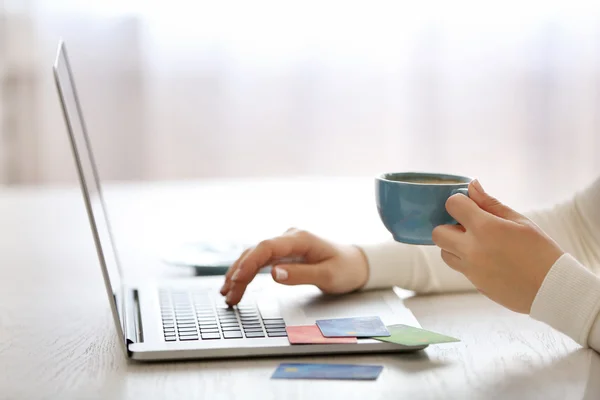 E-commerce concept. Woman with credit card, laptop and cup of coffee, close up