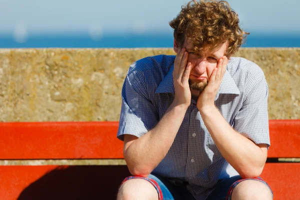 Tired exhausted man sitting on bench by sea ocean.