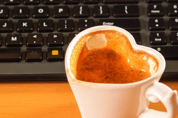 Cup of coffee next to computer keyboard.