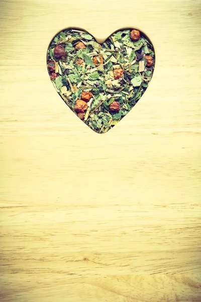 Dried herb leaves heart shaped on wooden surface