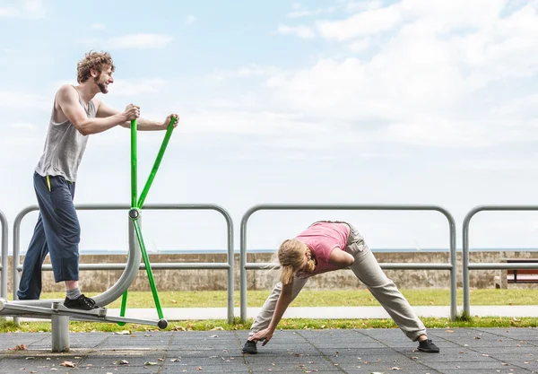 Man exercising on elliptical trainer and woman.