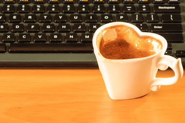 Cup of coffee next to computer keyboard