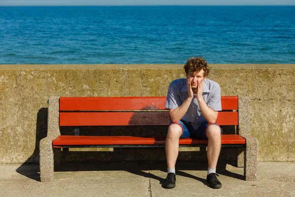 Tired exhausted man sitting on bench by sea ocean.