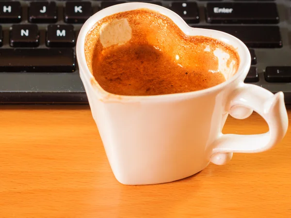 Cup of coffee next to computer keyboard.