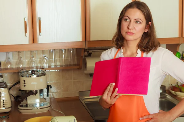 Housewife with cookbook in kitchen.