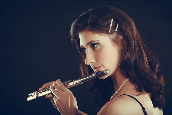 Woman playing transverse flute on black.