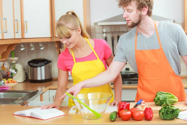 Couple cooking in kitchen reading cookbook