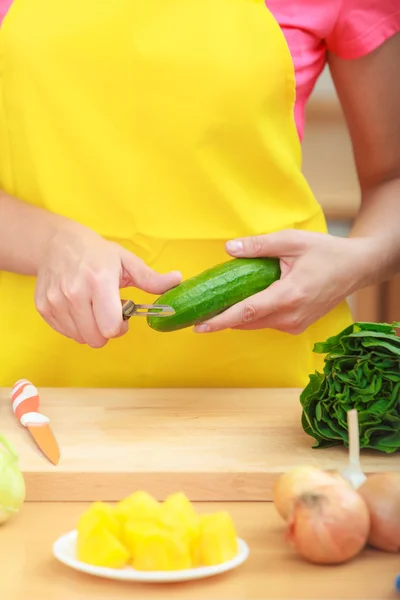 Woman preparing vegetables salad peeling cucumber