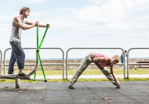 Man exercising on elliptical trainer and woman.