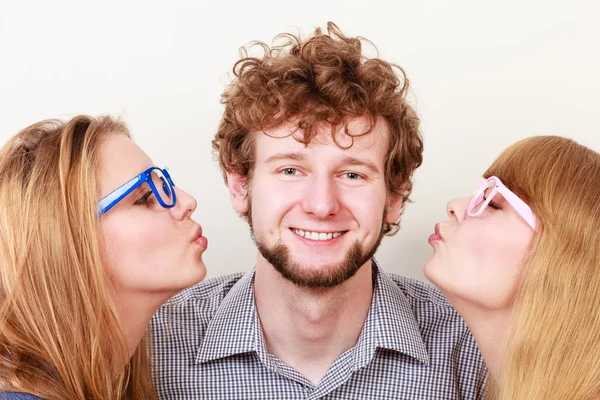 Two pretty young women kissing handsome man.