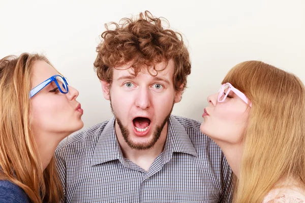 Two pretty young women kissing handsome man.