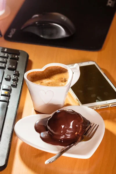 Cup of coffee and chocolate cake next to computer.