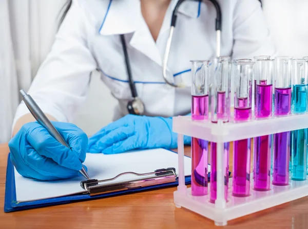 Doctor writes beside test tubes standing