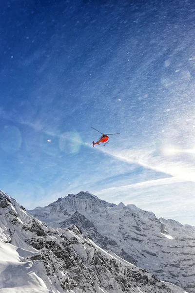 Red helicopter in flight in winter alps with snow powder streams
