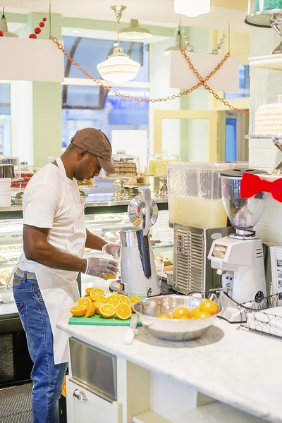 Black man extracting orange juice in cafe