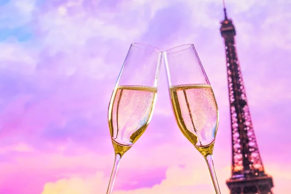 A pair of champagne flutes with golden bubbles on sunset blur tower Eiffel background