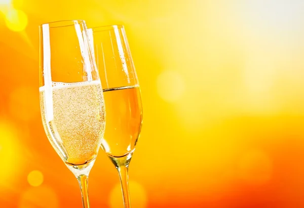 Champagne flutes with golden bubbles on golden light background