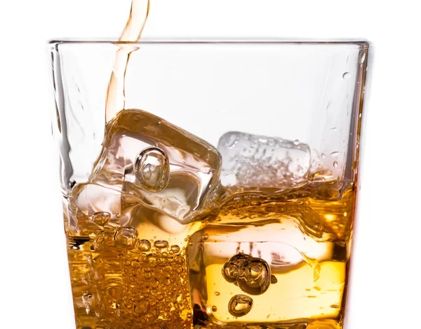 Detail of pouring scotch whiskey in glass with ice cubes on white
