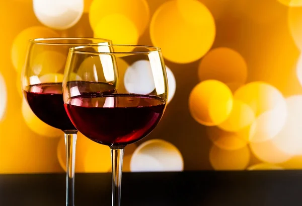 Two red wine glasses on wood table against golden bokeh lights background
