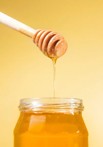 Honey jar on golden background with wooden honey dipper on top with drop honey