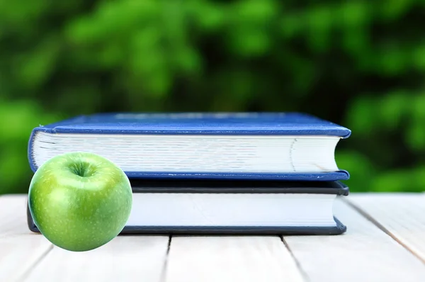 Green Apple and Books on Wooden Table on Nature Background