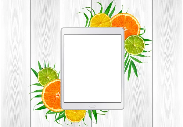 Tablet pc in green fern leaves and citrus fruits; orange, lime;