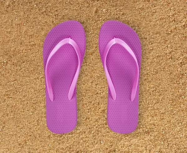 Pink beach shoes over yellow sand