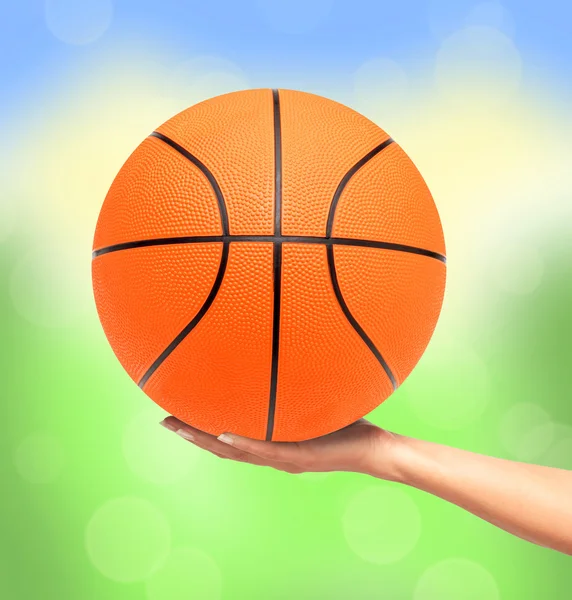 Basketball ball on woman hand over bright nature background