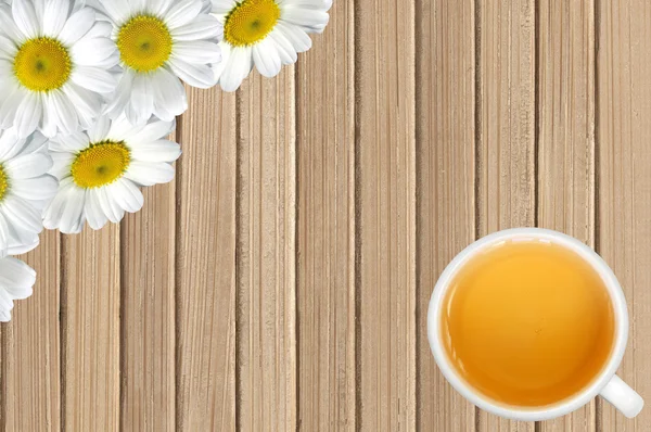 White chamomile flowers and tea cup on wooden table background