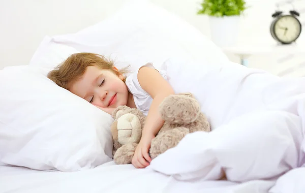 Child little girl sleeps in the bed with teddy bear