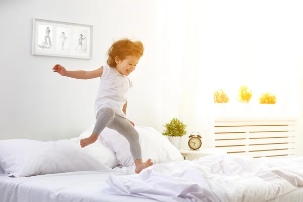 Happy child girl jumps and plays bed