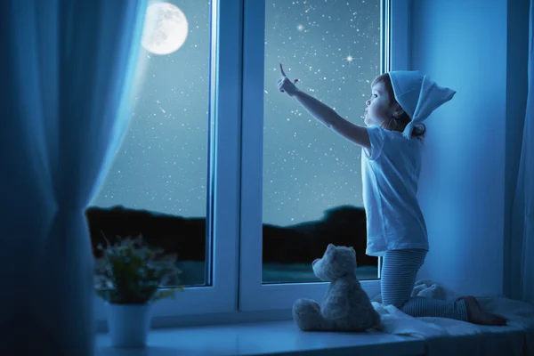 Child little girl at window dreaming and admiring starry sky at