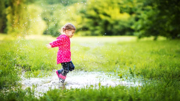 Happy child girl running and jumping in puddles after rain