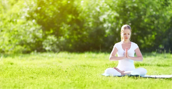 Young woman enjoying meditation and yoga on green grass in summe