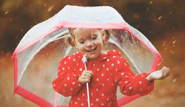 Happy child girl laughing with an umbrella in rain