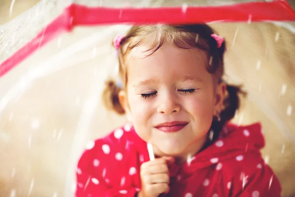 Happy child girl laughing with an umbrella in rain